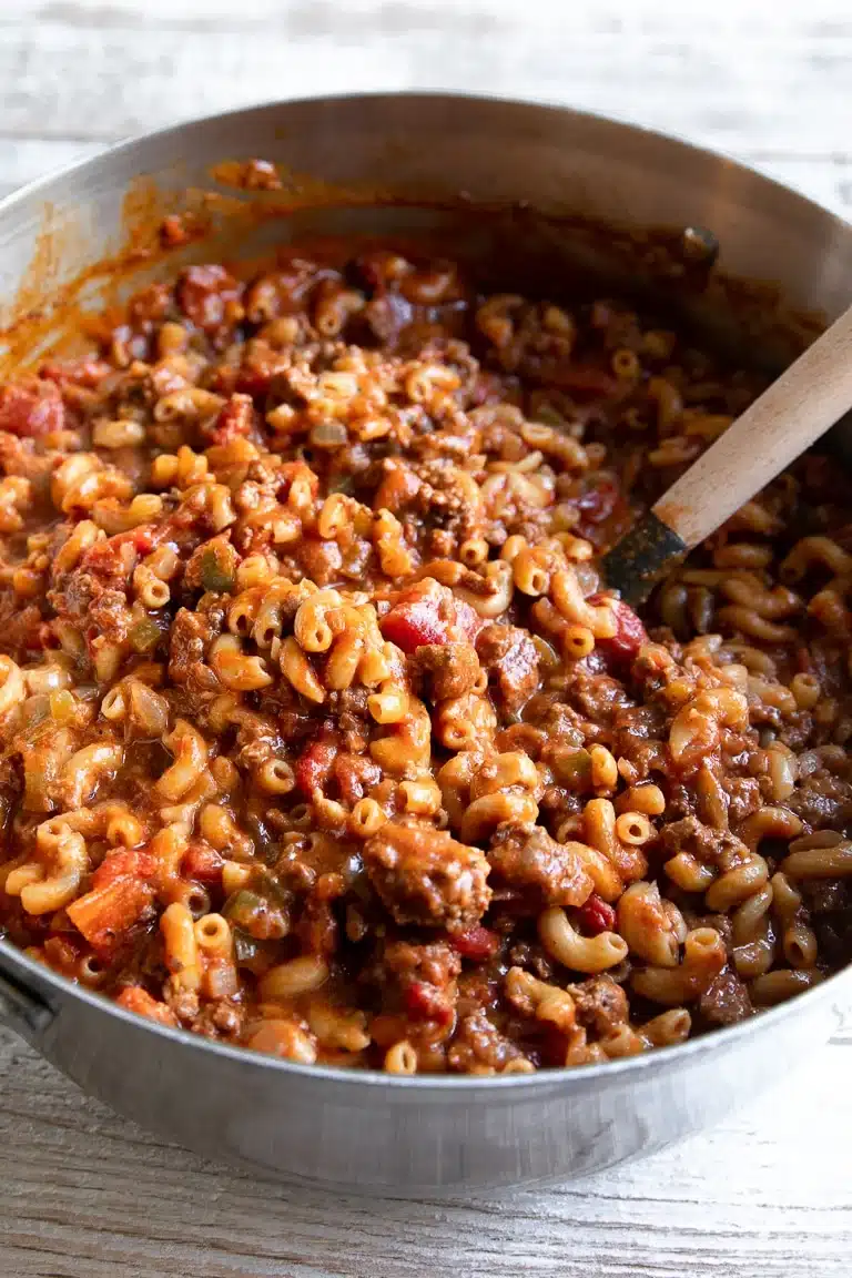 Overhead view of American goulash with ground beef, elbow macaroni, and bell peppers in a stainless steel skillet.