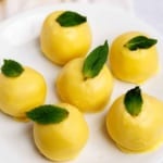 Yellow lemon truffles garnished with fresh mint, grouped closely on a white serving plate.