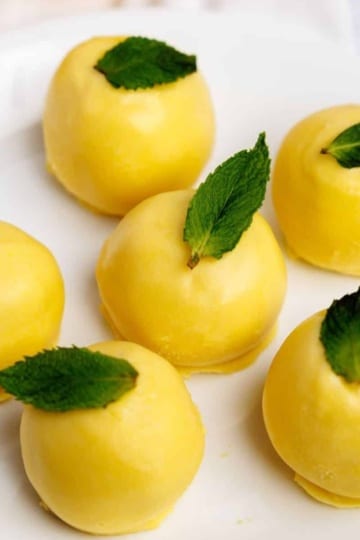 Yellow lemon truffles garnished with fresh mint, grouped closely on a white serving plate.