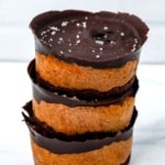 Stack of three mini pumpkin chocolate cheesecakes with a chocolate crust, topped with dark chocolate and sea salt.