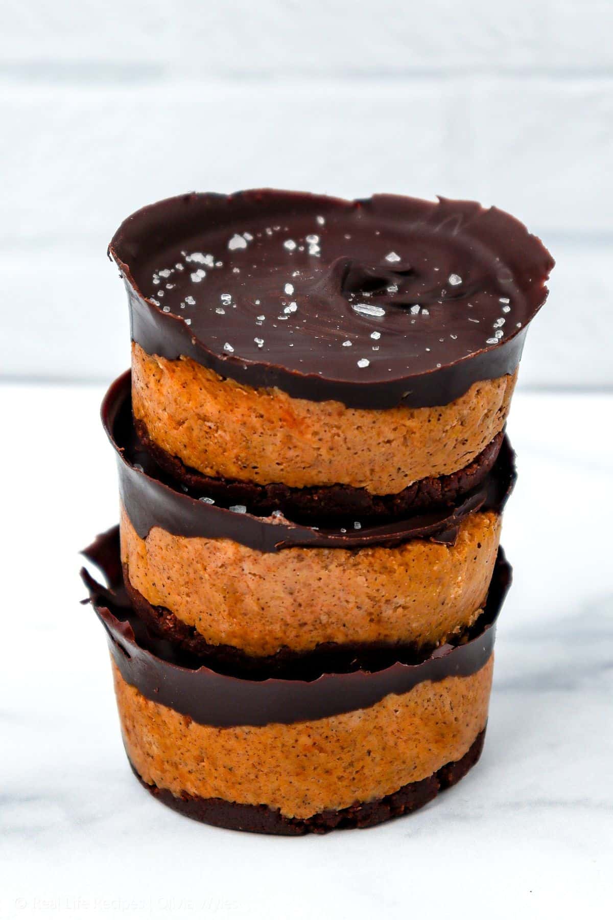 Stack of three mini pumpkin chocolate cheesecakes with a chocolate crust, topped with dark chocolate and sea salt.