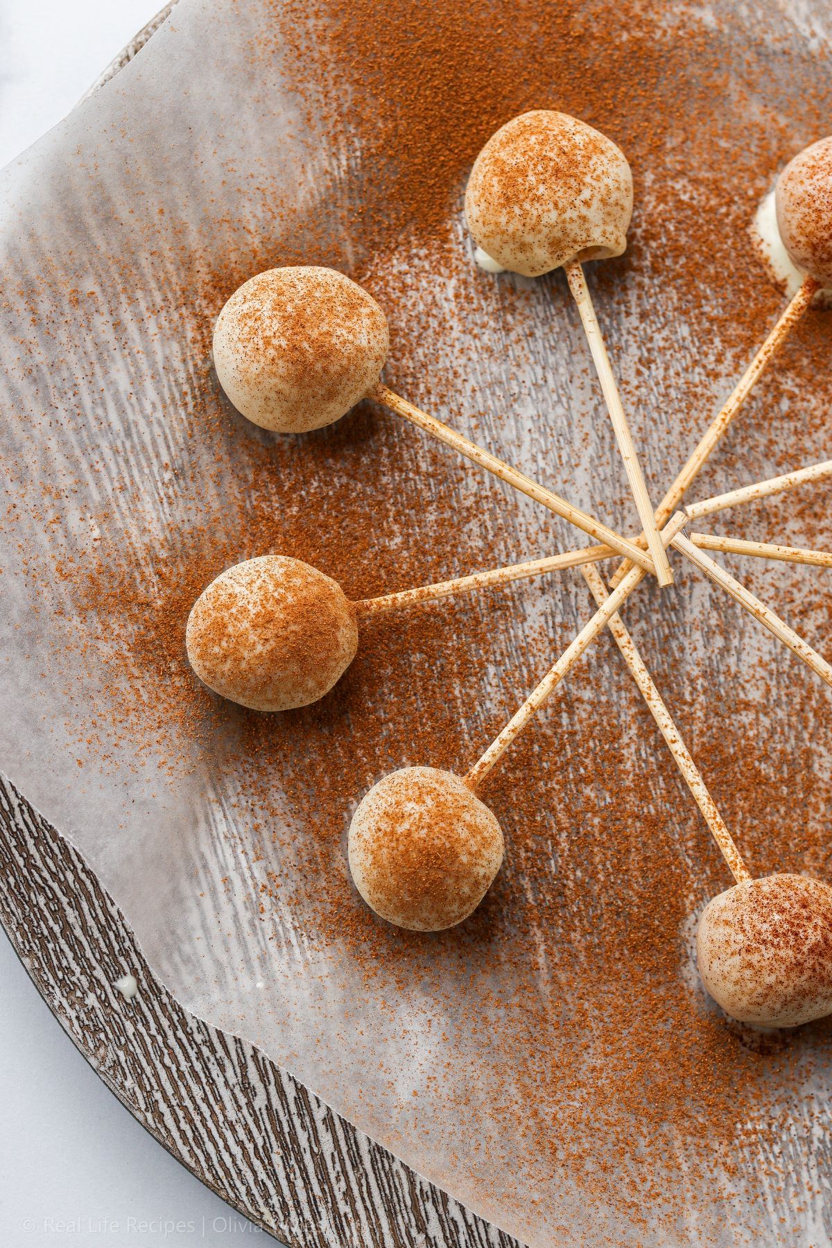 White chocolate coated pumpkin cheesecake pops dusted with pumpkin spice, fanned out on a marbled tray.
