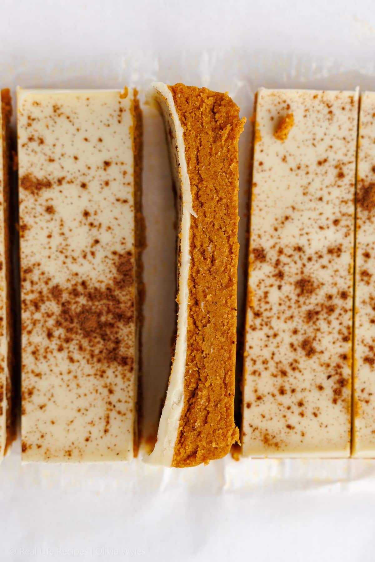 Sliced pumpkin protein bars in a row, one turned on its side to show the pumpkin inside and coating