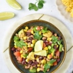 Overhead view of Cowboy Caviar bean salad in a bowl with lime wedges, cilantro, and tortilla chips nearby.