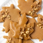 Glazed maple leaf cookies with chopped walnuts arranged on a white plate, ready to serve.