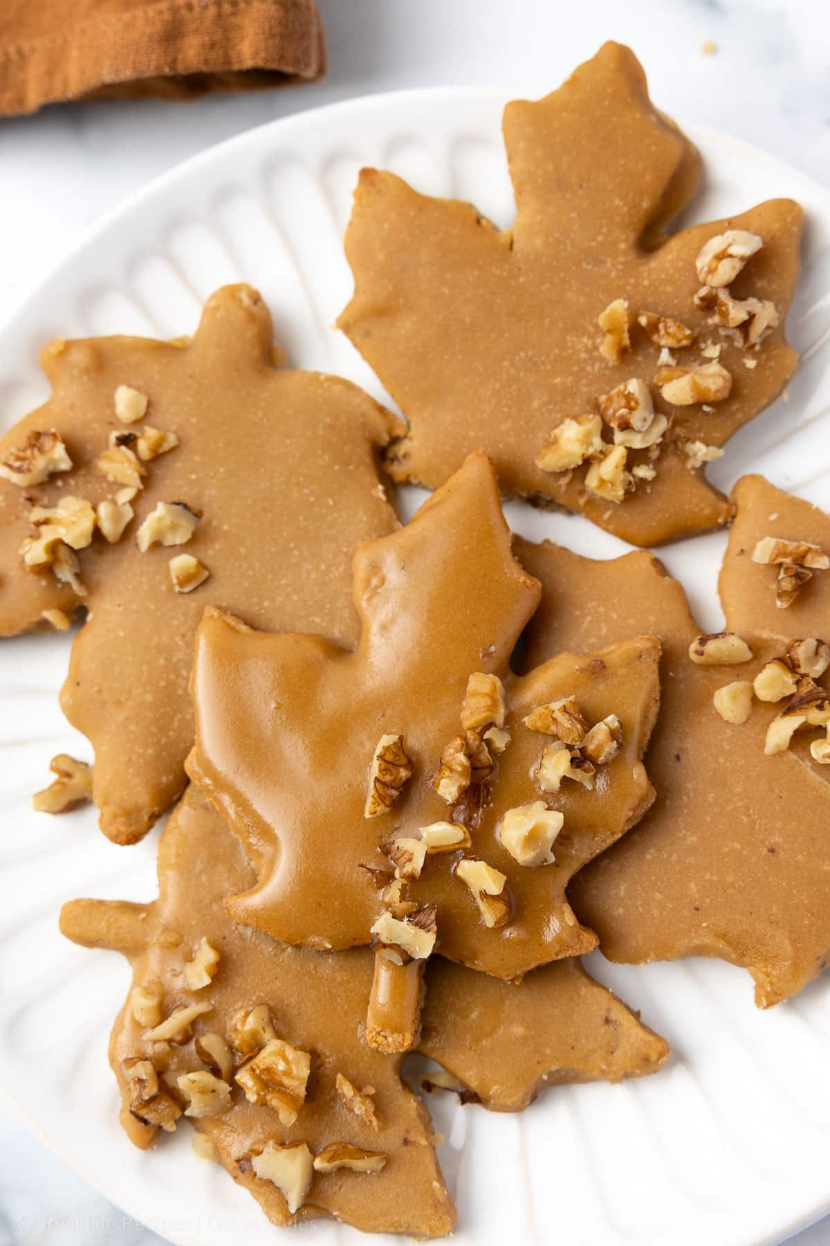 Glazed maple leaf cookies with chopped walnuts arranged on a white plate, ready to serve.