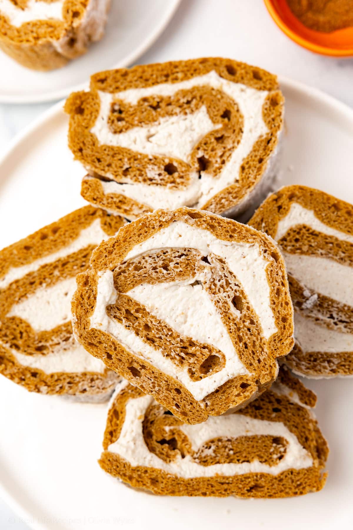 Sliced gluten-free sugar-free pumpkin roll on a white plate showing the cream cheese swirl inside.
