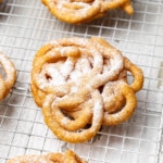 Close-up of a mini funnel cake dusted with powdered sugar sitting on a wire cooling rack.