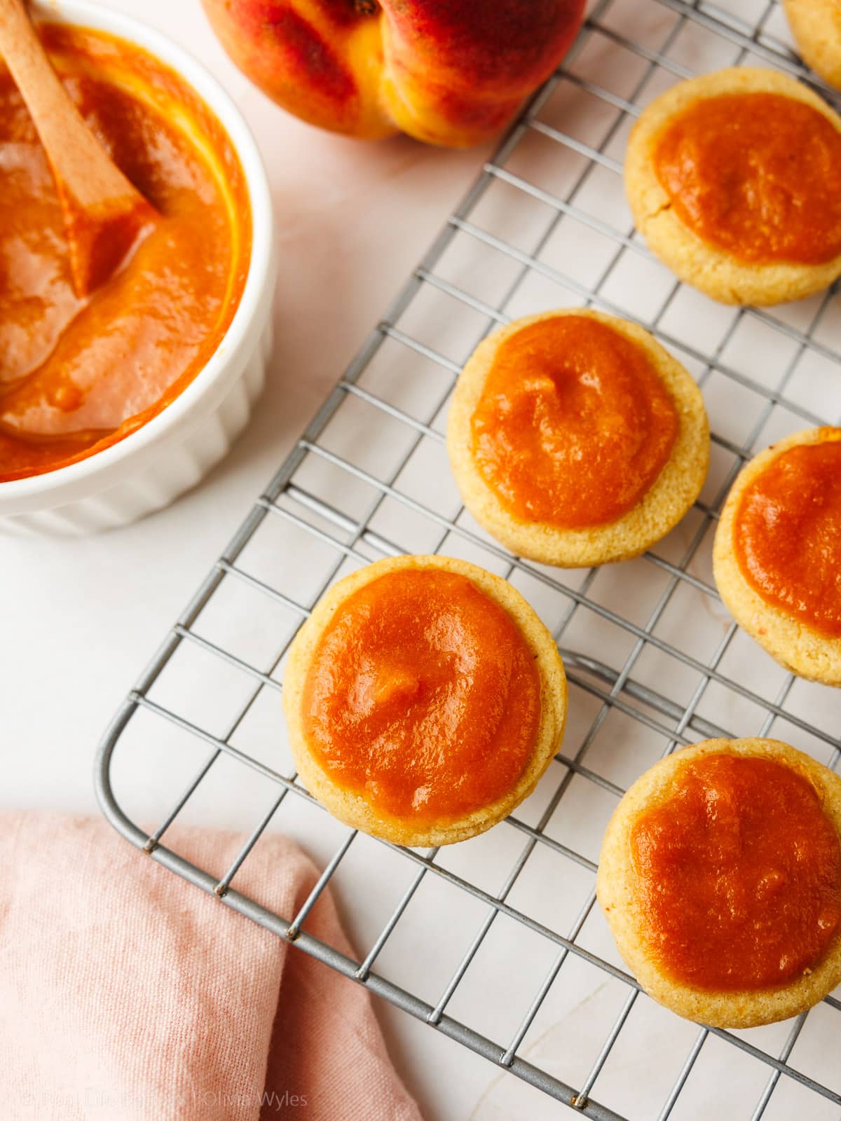 Baked peach cookies topped with glossy peach butter, cooling on a wire rack.