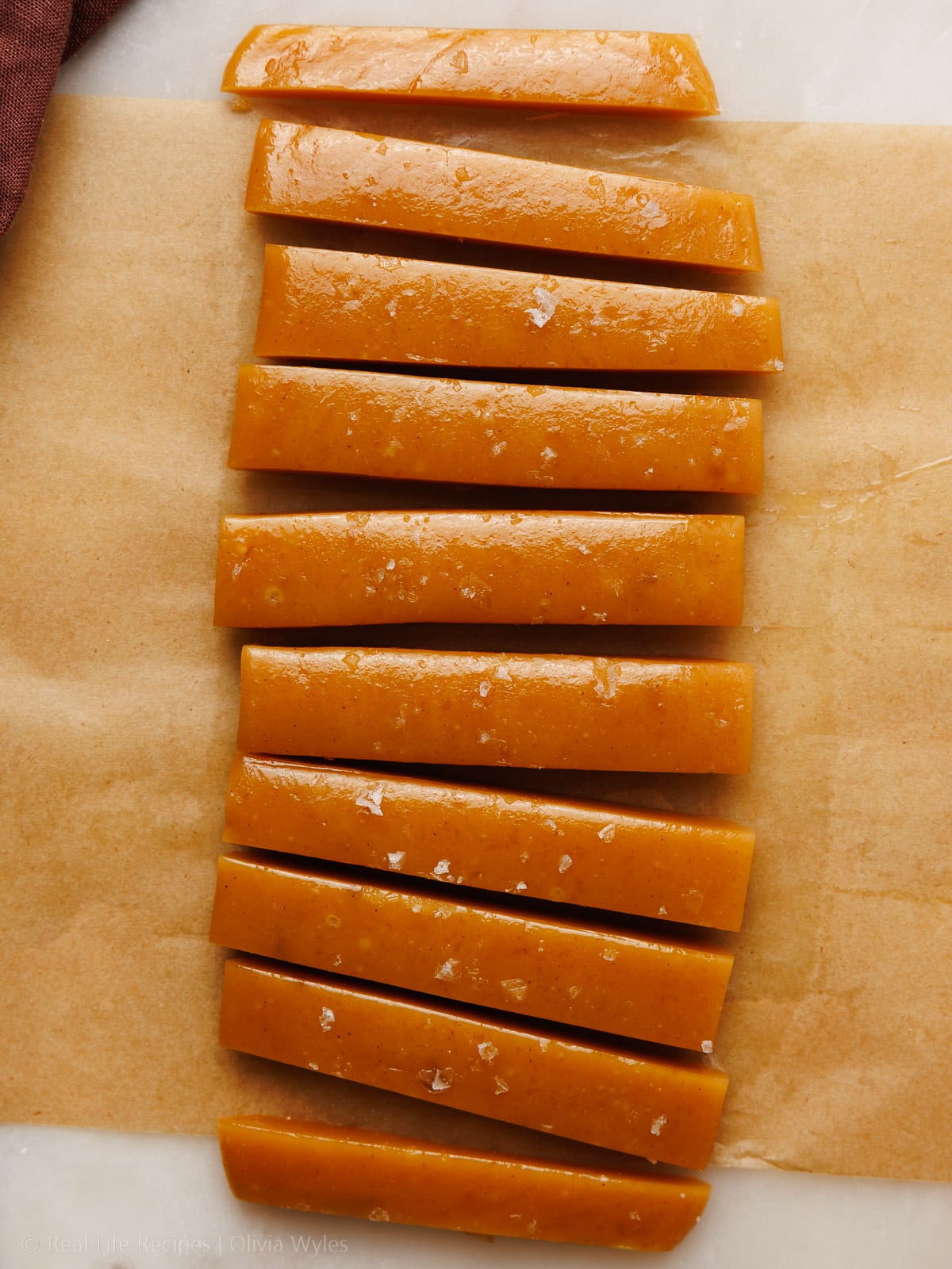 sliced apple caramel candy sprinkled with sea salt on brown parchment paper overhead view
